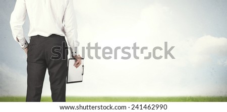 Businessman from the back in front of an empty meadow 