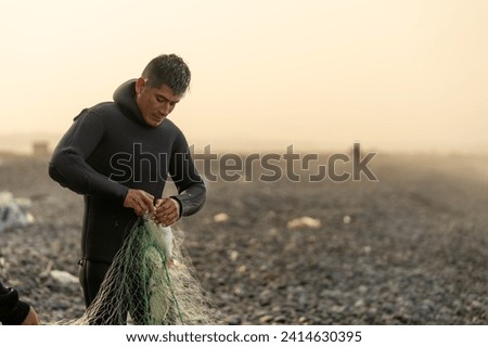 Man in wetsuit collecting fish from a net on the beach