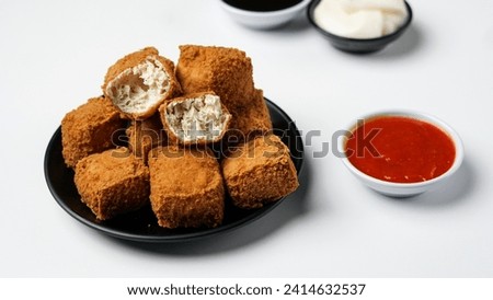 Fried tofu on a black plate with three sauces of mayonnaise, chili and sweet soy sauce on a white background