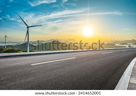 Asphalt highway and wind turbines with mountain natural landscape at sunset. High Angle view. Royalty-Free Stock Photo #2414652001