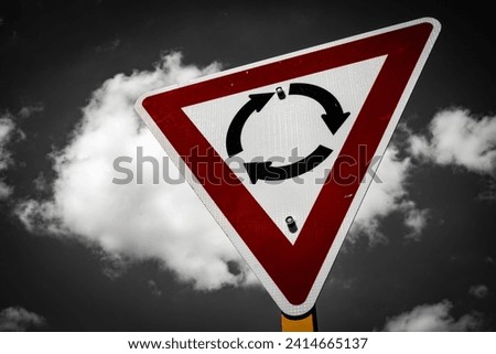 A road sign of a roundabout in colour in a black and white background with mighty clouds