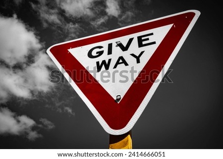 A road sign of a give way in colour in a black and white background with mighty clouds