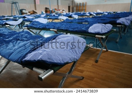 Cots with sleeping bags are placed in the school gym during an emergency Royalty-Free Stock Photo #2414673839