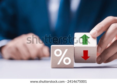 Business and finance concept. Businessman holding wooden block with percent and up or down arrow icon for mortgage and loan rates. Interest rate, stocks, ranking. 