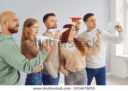Team of confident young people playing with paper planes. Group of ambitious motivated men and women in casual clothes preparing to fly paper airplanes. Dream, confidence, success, leadership concepts Royalty-Free Stock Photo #2414676055