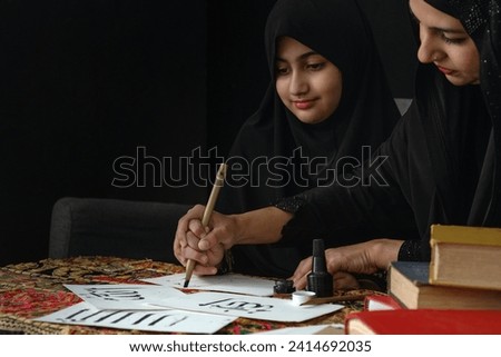 Muslim Arab woman teaching girl to write Arabic hand writing with ink, Arabic letters mean the name of god "Allah" and "Prophet Muhammad", black background, khat writing  