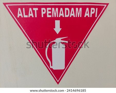 An acrylic fire hydrant nameplate in Indonesian is installed on a white wall as a background to provide information or as a sign for the location of fire extinguishers with a red base and white font.
