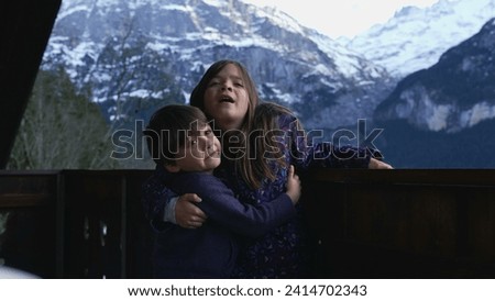 Young Siblings Embracing on Chalet Balcony for Photo in the Alps, small brother hugging sister, family love and affection
