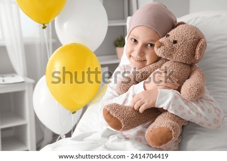 Little girl after chemotherapy with toy bear lying in bed at hospital. International Childhood Cancer Day Royalty-Free Stock Photo #2414704419