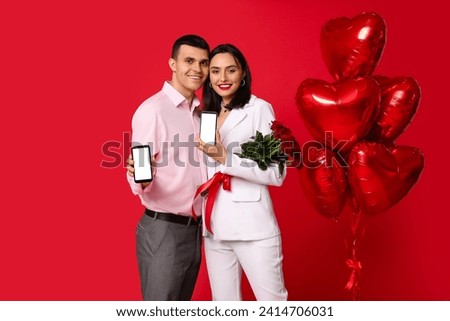 Young couple with mobile phones, bouquet of roses and heart-shaped air balloons on red background. Online dating