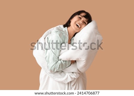 Beautiful young woman in pajamas with blanket on brown background