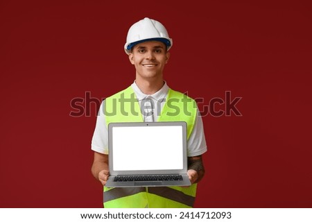 Young male engineer showing laptop with blank screen on red background