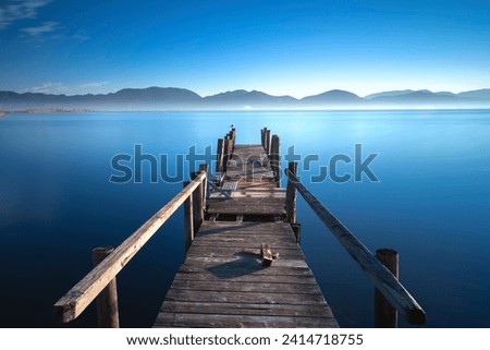 Wooden pier or jetty on the lake at sunrise. Lake Massaciuccoli, Torre del Lago Puccini, Versilia, Tuscany region, Italy, Europe Royalty-Free Stock Photo #2414718755