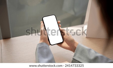 Close-up image of a woman using her smartphone at a table indoors. a white-screen smartphone mockup. people and wireless technology concepts