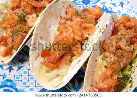 tacos with salmon and tomato on a blue plate on a white background