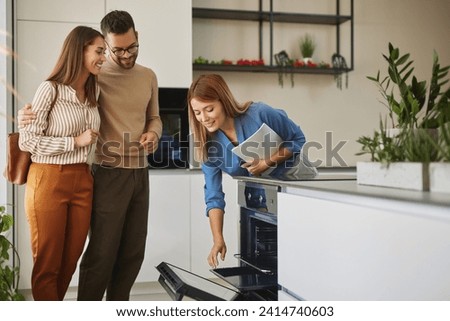 Female shop assistant helping young couple choose new electric stove Royalty-Free Stock Photo #2414740603