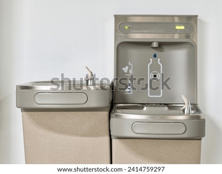 Water bottle refilling station with twin drinking fountains isolated by a plain white wall. Touchless automated eco friendly technology. Royalty-Free Stock Photo #2414759297