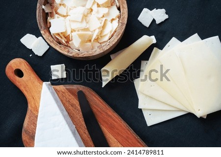 Parmesan, Camembert, Gouda cheese on a wooden board and bowl on a dark background