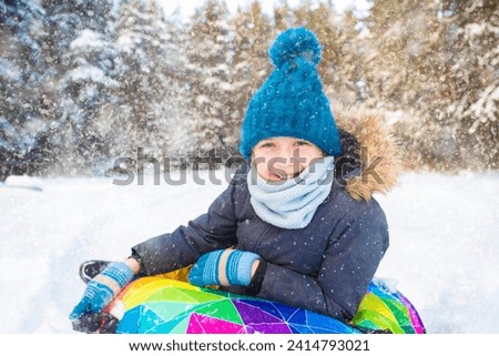 Cute little boy sliding on snow tube in winter forest. Happy childhood