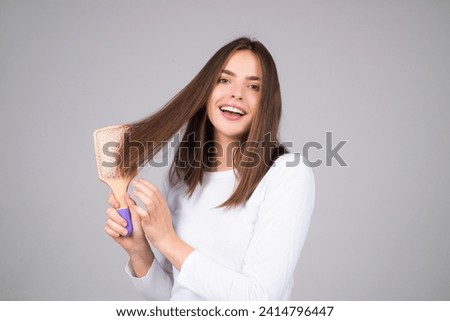 Beautiful model girl with comb brushing hair. Beauty woman with straight hair on studio background. Woman holding hairbrush near face. Healthy hair. Hairstyle and hair care concept. Shiny hairs. Royalty-Free Stock Photo #2414796447