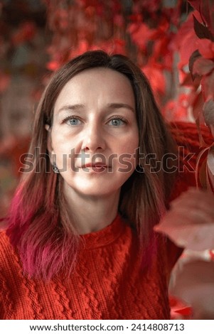 A woman in a bright terracotta dress against a background of red and yellow autumn grape leaves. Autumn.