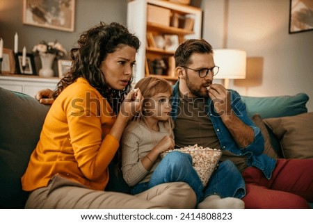 A loving family sitting together, watching a scary movie, and indulging in delicious popcorn in their cozy living room