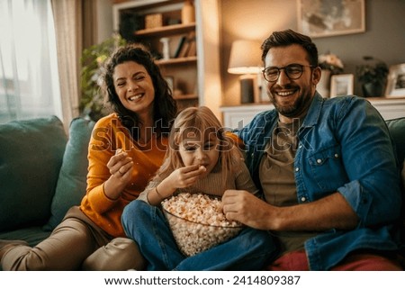 Dad, mom, and daughter enjoying a cinematic experience with smiles and popcorn in the living room