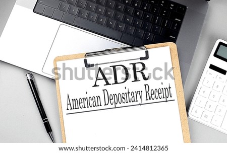 Paper clipboard with ADR on laptop with pen and calculator, business