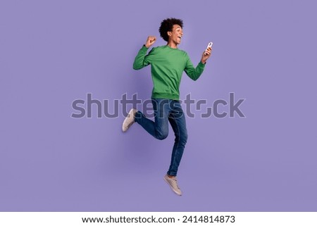 Full length photo of excited lucky man dressed green sweater jumping winning game device empty space isolated violet color background