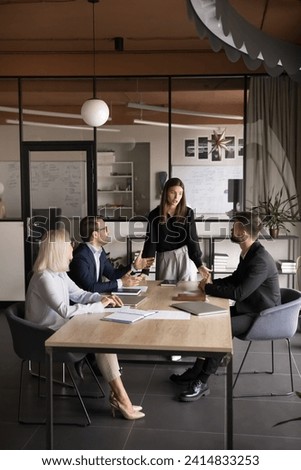Young team manager woman talking to business colleagues at large meeting table, presenting project plan. Employees discussing collaboration, group tasks, working together Royalty-Free Stock Photo #2414833253