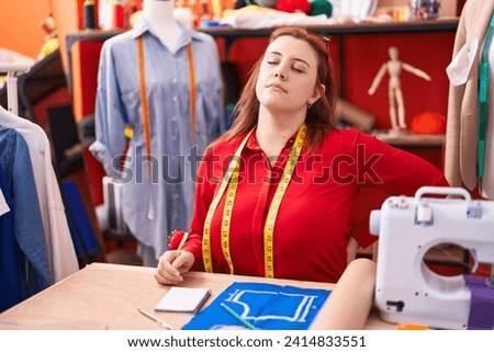Young beautiful plus size woman tailor stressed sitting on table at atelier Royalty-Free Stock Photo #2414833551