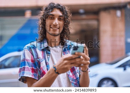 Young hispanic man smiling confident using smartphone at street Royalty-Free Stock Photo #2414839893