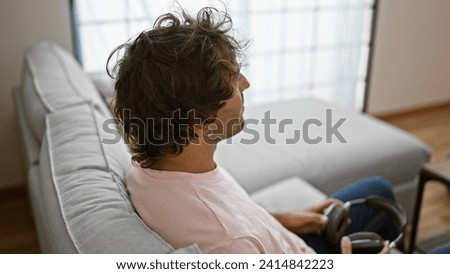 Handsome hispanic man relaxing on a couch in a modern apartment interior, holding headphones.