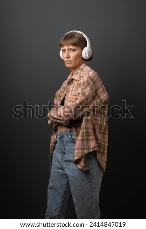 Beautiful young woman in white headphones listen music and dance with a bob hairstyle in a plaid shirt on a dark background