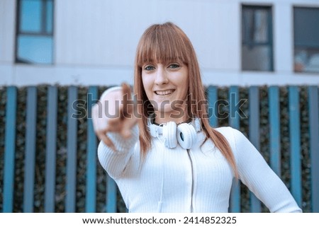 Confident and smiling young woman pointing her finger forward outdoors.