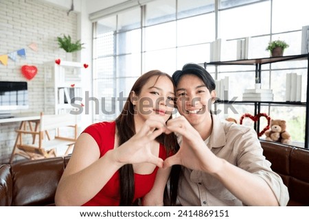Asian cute couple start dating and show heart hand sign gesture when girlfriend and boyfriend take a photo while looking at camera with soulmate lover concept in living room at the studio house