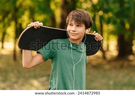Outdoors portrait of a cool teen boy with earphones holding his skateboard.
