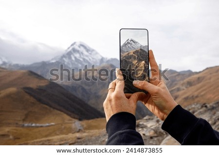 A hand holds a smartphone capturing the breathtaking view of a majestic mountain landscape