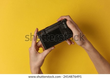 Hands holding a modern mirrorless camera with the screen facing up on a yellow background