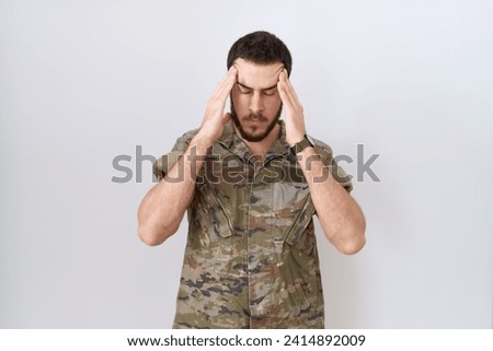 Young hispanic man wearing camouflage army uniform with hand on head for pain in head because stress. suffering migraine. 