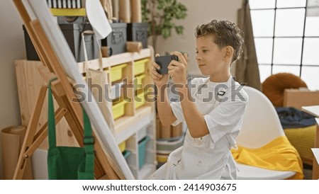 Adorable blond boy artist, smiling as he's taking a picture in an art studio, ready to draw his masterpiece on canvas