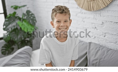 Adorable blond boy, radiating confidence, happily sitting on a cozy bed in a sunny bedroom, enjoying a relaxing morning indoors