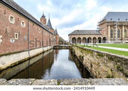 Straight moat between Alden Biesen castle and outer courtyard, building with arched hallway with pillars, brick walls and gable roof in background, 16th century, cloudy day in Bilzen, Limburg, Belgium Royalty-Free Stock Photo #2414910449