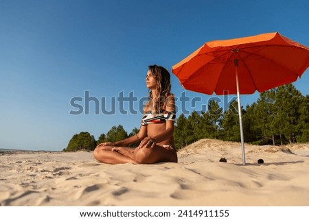 Young tanned woman wearing bikini meditates in lotus position alone on the beach