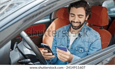 Young hispanic man shopping with smartphone and credit card sitting on car at street