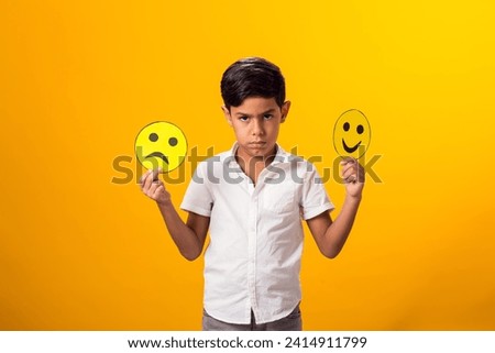 Upset boy holding happy and sad faces on two pieces of memo paper.