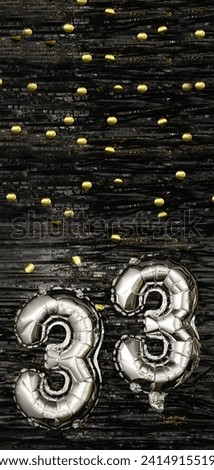 Silver foil balloon number 33 on a background of black tinsel with gold confetti. Birthday card, inscription thirty-third. Anniversary event. Vertical banner. copy space.