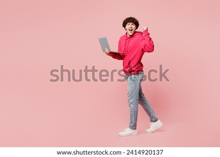 Full body young Caucasian IT man he wears hoody casual clothes hold use work on laptop pc computer do winner gesture isolated on plain pastel light pink background studio portrait. Lifestyle concept