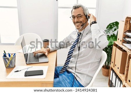 Middle age grey-haired man call center agent smiling confident working at office Royalty-Free Stock Photo #2414924381