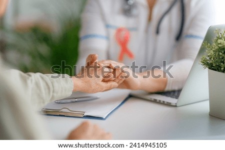Pink ribbon for breast cancer awareness. Female patient listening to doctor in medical office. Support people living with tumor illness. Royalty-Free Stock Photo #2414945105